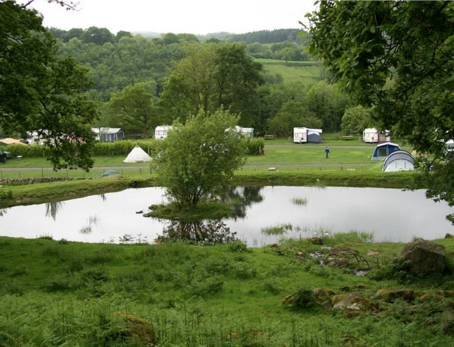 A green field with a large lake in the middle. Across from the lake there are some tents