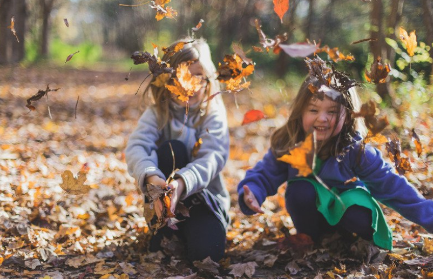 Two young girls throwing autumn leaves from the ground