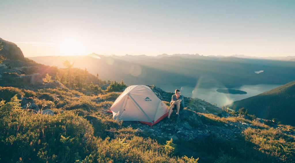 A man sat with his tent on a sunny mountain