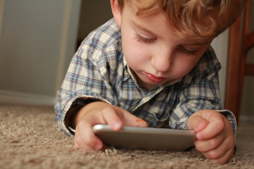 A boy laying on the carpet looking at an ipad 