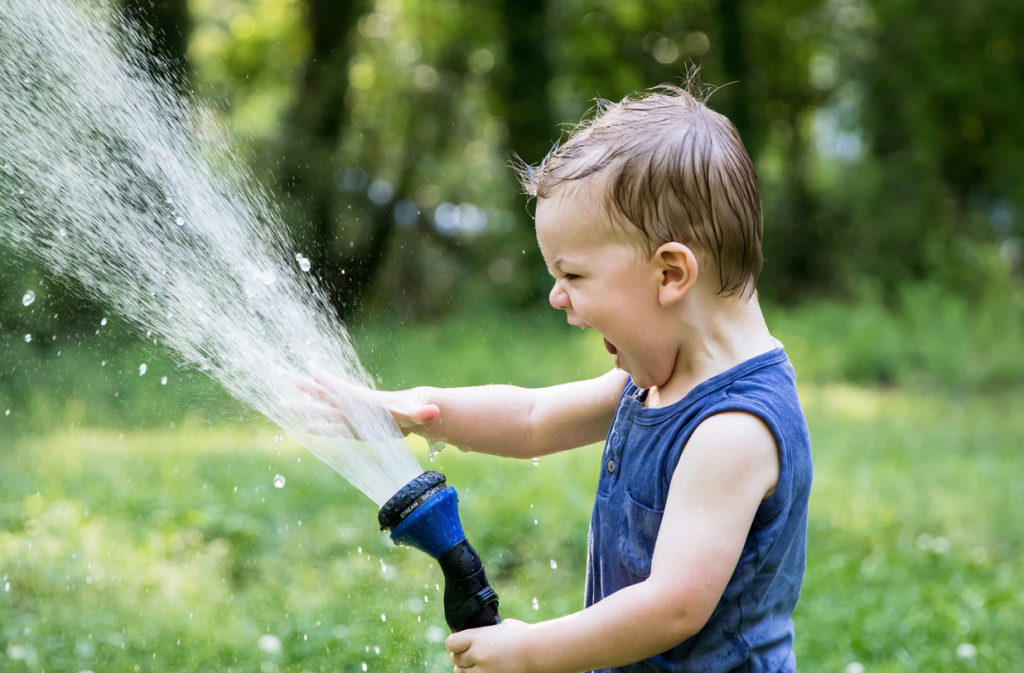 A toddler boy outside laughing and smiling with a water sprinkler