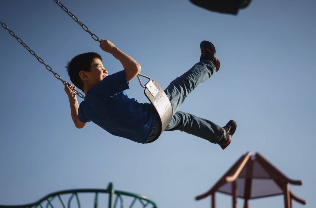 A young boy on a swing with his legs in the air