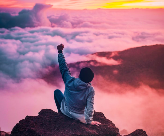 A man sat on a rock with his fist in the air in celebration