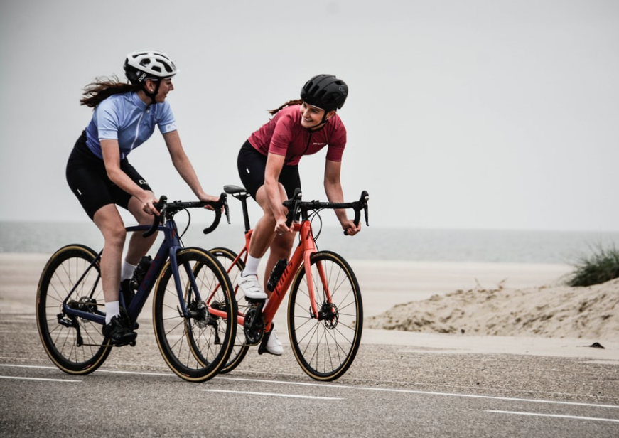 Two women cycling whilst smiling and looking at each other