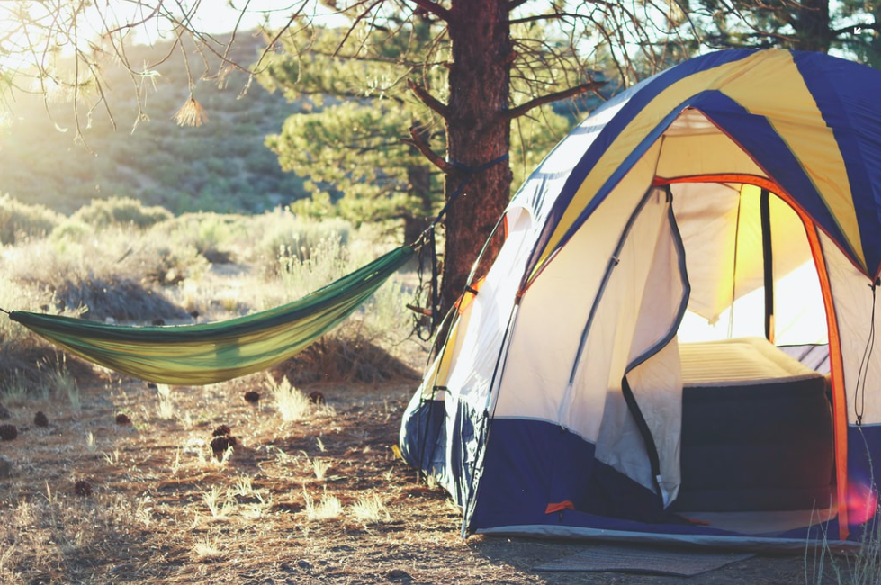 A tent and a hammock in the woods with the sun shining through the trees.