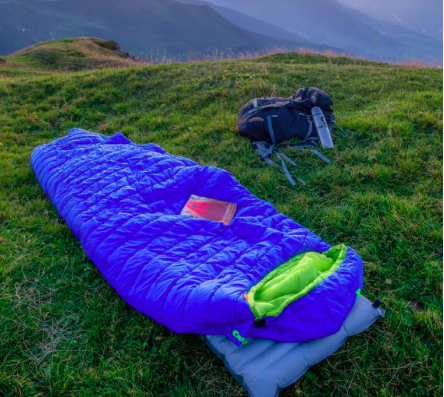 A blue sleeping bag and backpack on the grass.