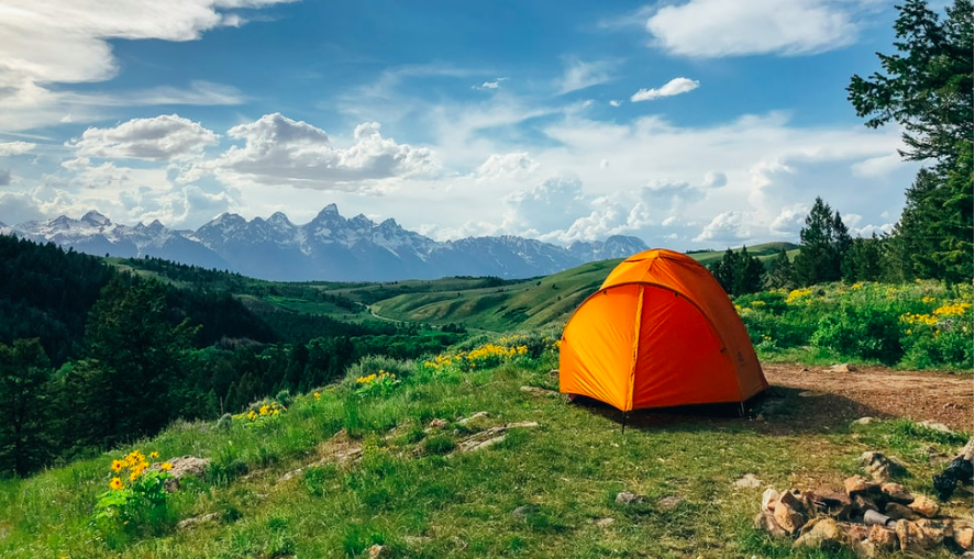 An orange tent set up on the grass wirh mountains and blue sky in the distance