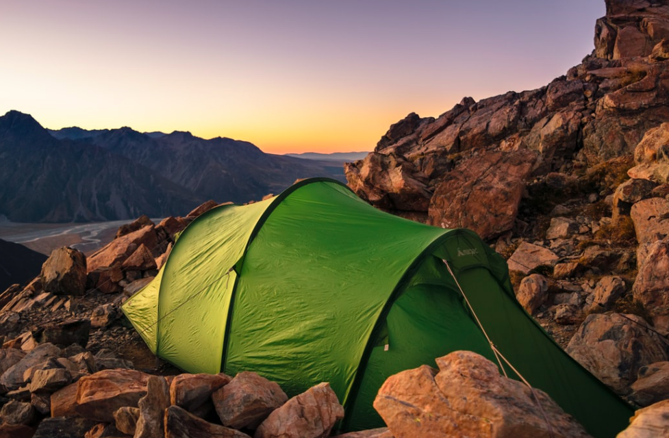 A green tent set up in a rocky mountain