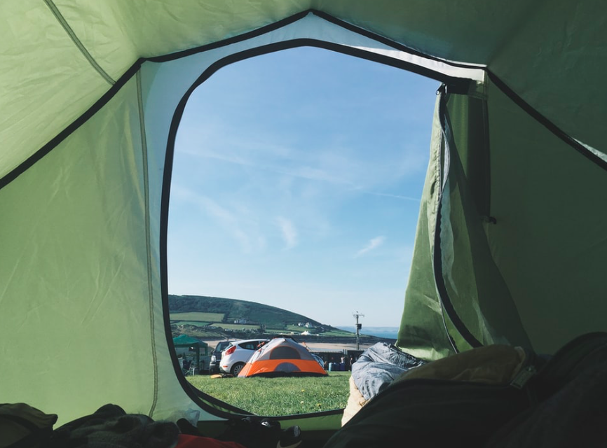 The view from inside a green tent, looking out at a blue sky