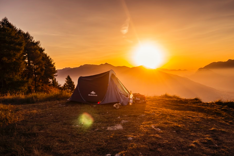 A quechua tent on the grass with an orange sunrise