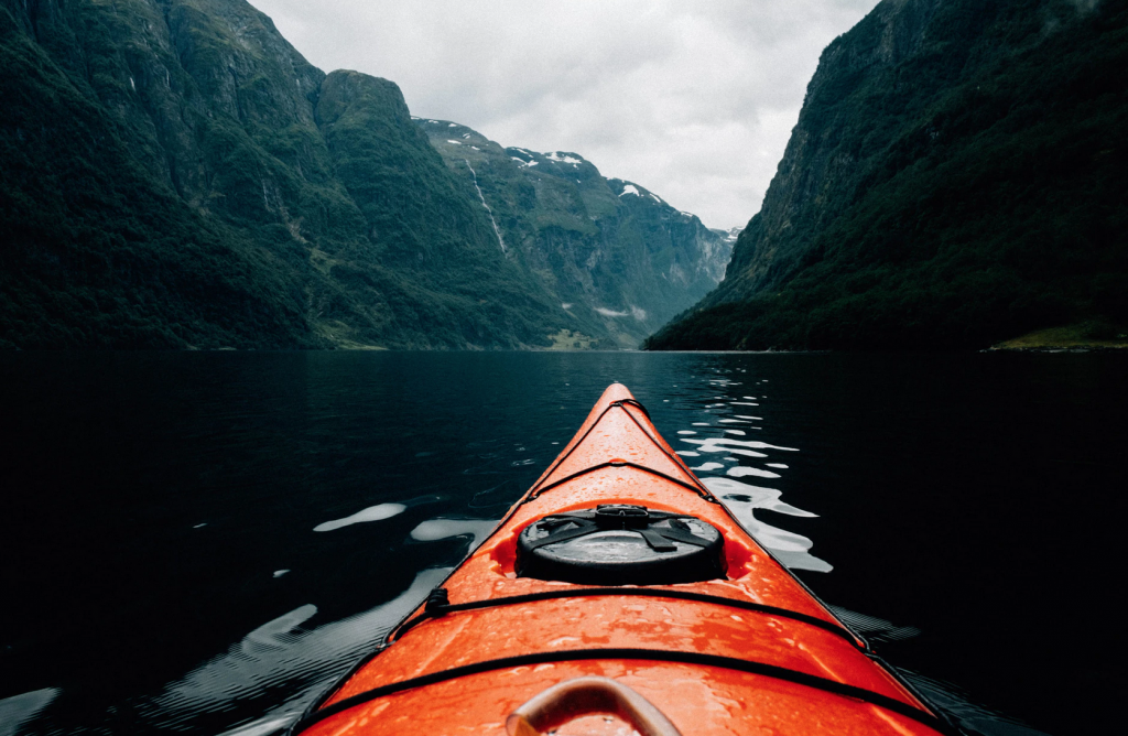 The end of an orange kayak in water surrounded by mountains