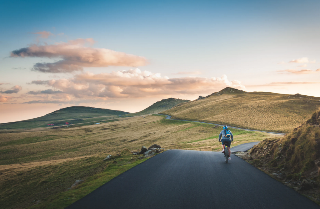 A person cycling along a road surrounded by green fields and hills