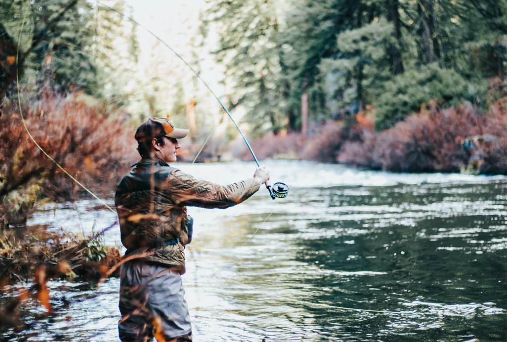 A man with a fishing rod swinging it into a lake