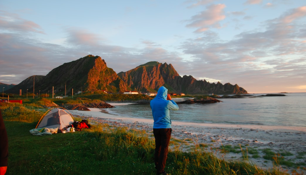 A man stood at the edge of the sea with a tent in the background