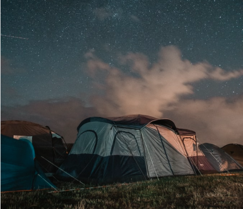 A grey tent on grass with a starry sky behind it