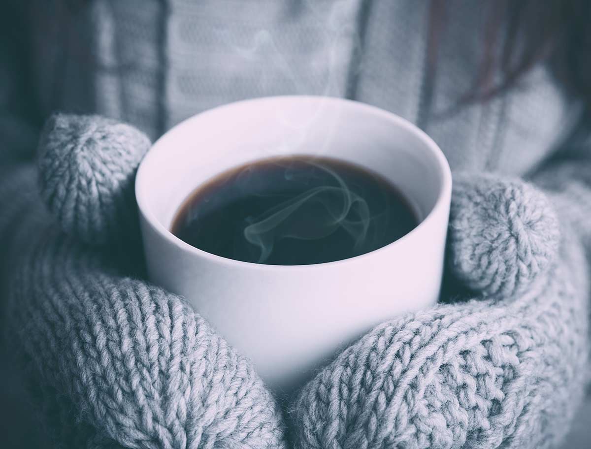 Gloved hands around a cup containing a hot drink